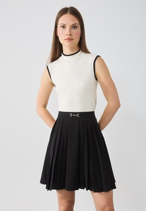 Fitted white sleeveless top with black trim paired with a black pleated skirt featuring a silver buckle accent at the waist.