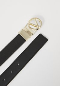 Curea neagră cu un finisaj texturat, având o cataramă circulară aurie cu un design de decupaj geometric; curea plată cu cinci găuri pentru ajustare.