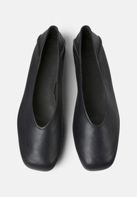 Ein Paar schwarze Leder-Slipper mit quadratischen Zehen, von oben gegen einen weißen Hintergrund gezeigt.