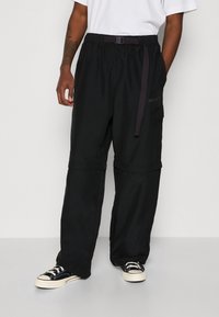 Černé cargo kalhoty vyrobené z odolné látky, s nastavitelným páskem, elastickým pasem a boční kapsou. Volný střih s odstřiženým designem.