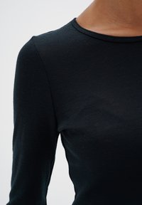 Svart långärmad topp med rund halsringning, tillverkad av ett slätt, lätt material; figurnära design med subtil textur.