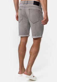 Shorts en denim gris avec des ourlets roulés, poches arrière, et une étiquette en cuir noir à la taille, associés à des sandales blanches à enfiler.