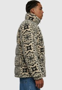 Puffer-takki vaaleassa ja mustassa, tekstuurilla ja kuviollisella fleece-pinnalla, korkealla kauluksella ja ylisuurilla mitoituksilla. Hihojen resorit ovat ribbikudosta.