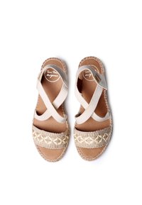Beige espadrilles sandaalit, joissa on ristiin menevät hihnat, kudottua juteeta varpaan kohdalla ja litteä, teksturoitu pohja.