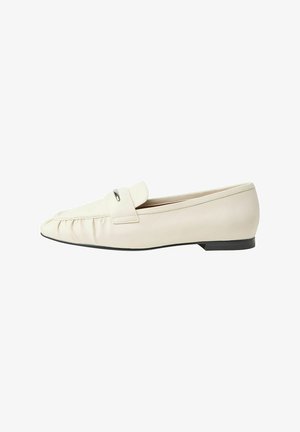 Mocassins en cuir beige avec un bout rond, présentant un devant texturé, une petite sangle et un accent métallique. Talon bas en caoutchouc noir.