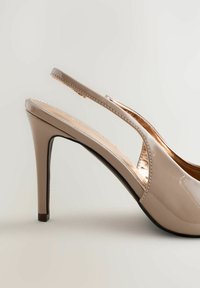 Tacón slingback de charol beige con puntera puntiaguda, tacón delgado y un detalle metálico dorado en el interior. Textura suave, diseño moderno.