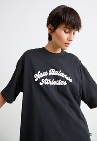 T-shirt en coton noir oversize avec le logo en cursive blanc "New Balance Athletics" sur le devant. Col rond et manches courtes.