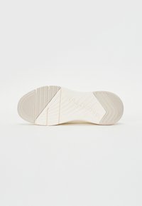 Semelle de chaussure en caoutchouc blanc avec des motifs texturés, y compris des lignes horizontales et diagonales, caractérisée par un talon incurvé et un logo en relief.