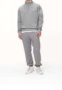 Felpa grigia con zip a un quarto, polsini a coste e logo. Abbinata a pantaloni sportivi coordinati con polsini elasticizzati e tasche frontali.
