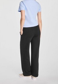 Jasnoniebieski krótki top z okrągłym dekoltem, w połączeniu z czarnymi dresami z bocznymi kieszeniami i luźnym krojem.