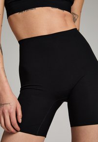 Shorts noirs taille haute sans coutures fabriqués en tissu extensible et lisse, avec un design épuré et des détails de couture discrets le long des coutures.