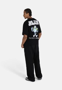 Black oversized t-shirt with cartoon character graphic on the back, white lettering, paired with black pants and sneakers.