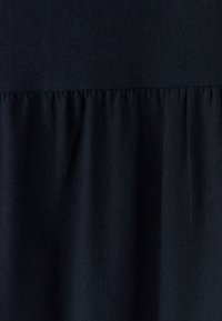 Tumma laivastonsininen kangas, jossa on sileä pinta ja joka esittää rypytettyä röyhelöyksityiskohtaa alareunassa. Yksinkertainen, minimalistinen muotoilu.