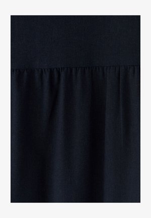 Tmavě námořnická látka s texturovaným povrchem. Na spodní části má plisovaný volán, který vytváří vrstvený vzhled. Hladká a jemná na dotek.