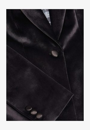 Blazer en velours noir avec une texture lisse, col cranté et trois boutons noirs au poignet. Présente une doublure intérieure à motif.