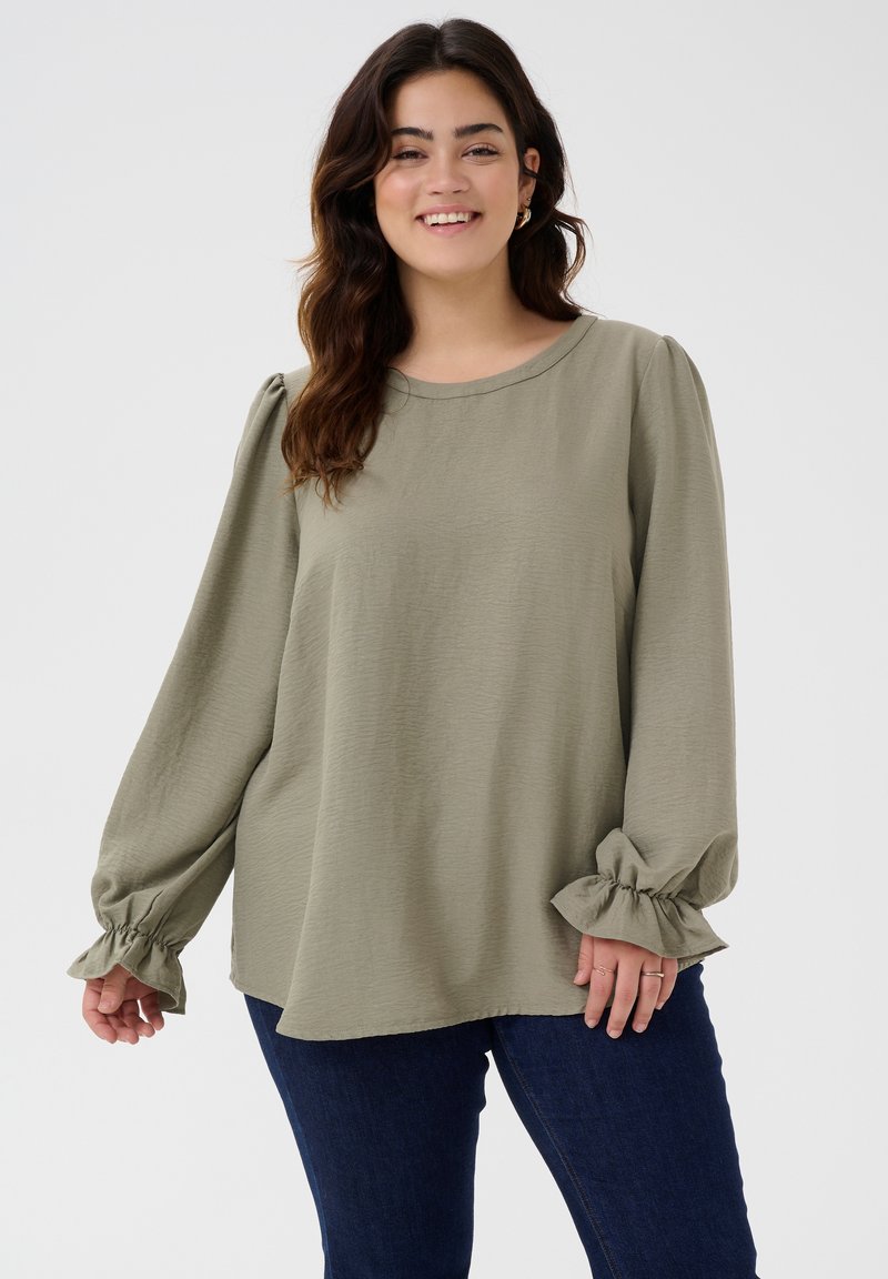 Loose-fitting olive green blouse with puffed long sleeves and gathered cuffs. Soft, textured fabric; rounded neckline. Worn with dark jeans.