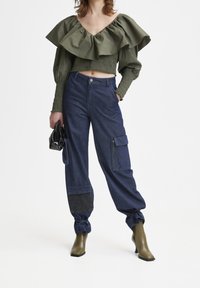 Top corto verde oliva con grandi rouches e dettagli smock, abbinato a pantaloni cargo in denim scuro con tasche con zip e polsini.
