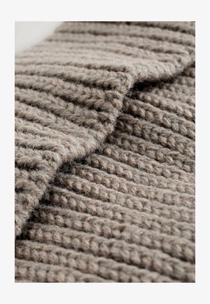 Strukturiert gewebter Stoff in einem sanften beigen Farbton, der ein geripptes Muster mit dickem, weichem Garn zeigt. Die Oberfläche wirkt flauschig und einladend.