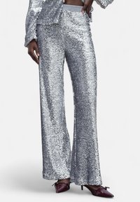 Pantaloni con paillettes argento dal design svasato, con una texture liscia e una cintura elastica, abbinati a scarpe a punta borgogna scuro.