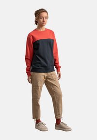 Felpa color-block in rosso e blu navy, in misto cotone, con colletto girocollo e maniche lunghe. Pantaloni cargo beige con tasche e dettagli di schizzi di vernice.