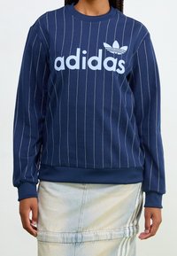 Navy blue sweatshirt with white vertical stripes, large "adidas" logo in light blue, ribbed crew neck, and cuffs. Soft, jersey fabric.