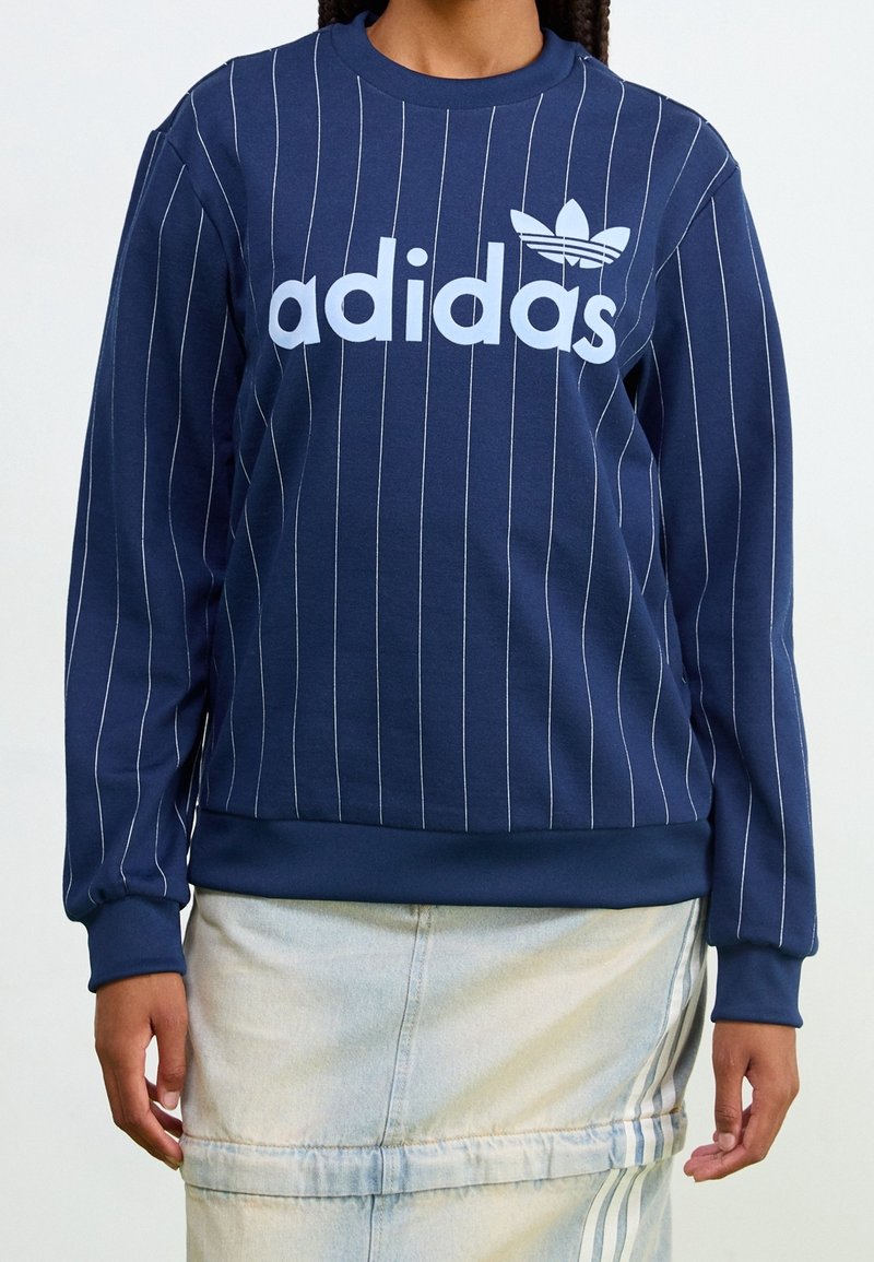 Navy blue sweatshirt with white vertical stripes, large "adidas" logo in light blue, ribbed crew neck, and cuffs. Soft, jersey fabric.