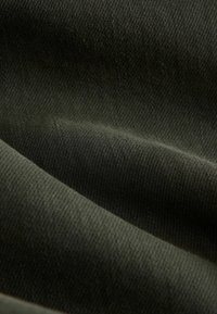Dunkelolivgrüner Stoff mit einer glatten, texturierten Oberfläche, die Falten aufweist, die subtile Schatten und Lichtreflexe erzeugen.
