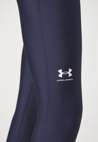 Tamno plave atletske tajice od glatkog, rastezljivog materijala. Sadrže kontrastne šavove i bijeli Under Armour logo na bedru.