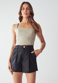 Světlé šedé krátké tričko se čtvercovým výstřihem a širokými ramínky, spárované s černými šortkami s vysokým pasem, které mají plisé a zlatý knoflík.