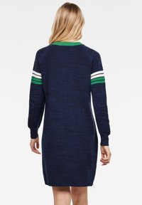 Laivastonsininen neulemekko, jossa on ribbikuvio, vihreät ja valkoiset raidat hihoissa sekä sivuvetoketjuyksityiskohta.