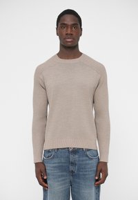 Beżowy sweter z dzianiny z długimi rękawami, o prążkowanej fakturze i okrągłym dekolcie, zestawiony z niebieskimi jeansami. Prosty i dopasowany fason.