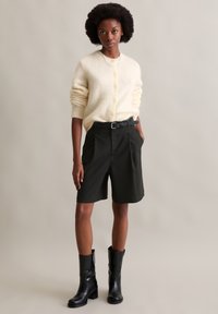 Kremowy, puszysty kardigan, czarne szorty dopasowane z zakładkami oraz czarne, wysokie kozaki na obcasie. Teksturalne materiały, nowoczesny design.