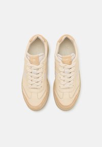 Kremfargede sneakers i glatt skinn, med teksturerte detaljer og beige snørebånd. Gull-logo på tungen, gummisåle og detaljer med stripe på siden.