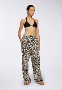 Top bikini nero abbinato a pantaloni larghi con stampa zebra beige e marrone, dotati di una vita regolabile con cordoncino e tasche laterali.