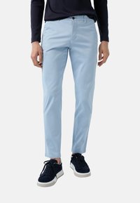 Lichtblauwe katoenen chinos met een slim fit, voorzien van een rits en knoopsluiting. Draagt met marineblauwe sneakers, wat een casual look creëert.