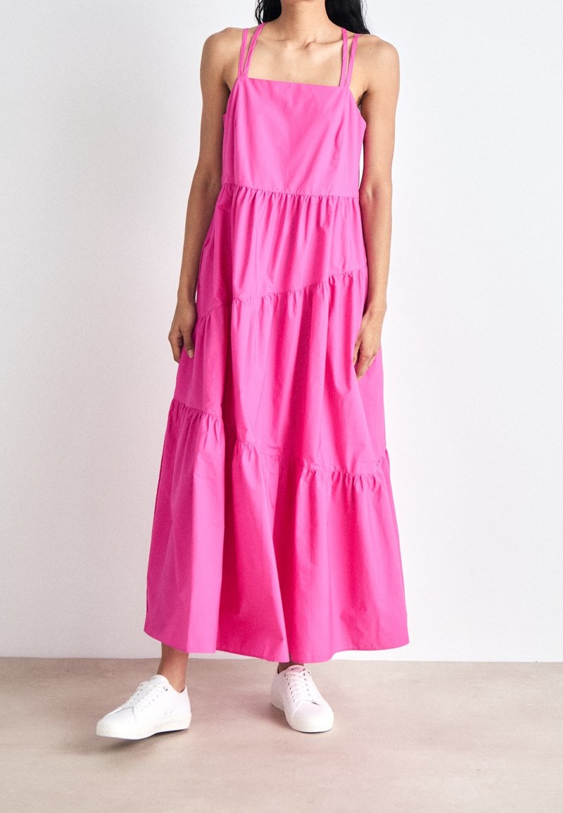 Różowa bawełniana sukienka maxi z regulowanymi ramiączkami, warstwowymi falbankami i luźnym krojem, zestawiona z białymi sneakersami.