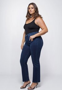 Donkerblauwe hoge taille jeans met een slim fit en subtiele stretch. Gecombineerd met een zwarte aansluitende tanktop en zwarte sandaaltjes met hak.