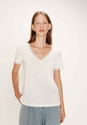 T-shirt blanc à manches courtes avec un col en V et un bord en dentelle au niveau du col et des manches, fabriqué dans un matériau texturé.