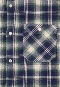 Camicia a quadri realizzata in tessuto di cotone. Motivo a scacchi verde e blu navy con accenti bianchi. Presenta una chiusura con bottoni davanti e una tasca sul petto.