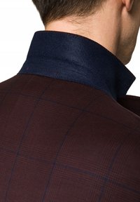 Ciemnoburgundowy żakiet w kratkę z teksturowanym granatowym kołnierzem. Posiada kontrastowe przeszycia wzdłuż krawędzi kołnierza.