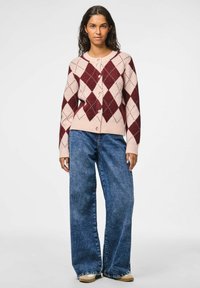 Rozā un bordo argyle raksta kardigāns ar apaļu kakla izgriezumu un pogu aizdari, kombinēts ar platajiem zilo džinsu biksēm.