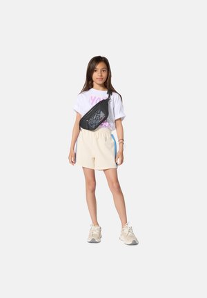 Schwarze Bauchtasche mit Blumenmuster, weißes T-Shirt mit pinkem Text, cremefarbene Shorts und beigen Sneakers. Modell steht vor einem schlichten Hintergrund.