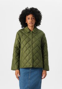 Veste matelassée verte avec une fermeture à boutons, grand col et motif en losanges texturé ; associée à une jupe en denim.