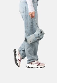 Sac à bandoulière en denim bleu clair avec poches zippées, fini avec une texture douce et des accessoires en métal. Porte avec un jean bleu clair et des baskets larges.