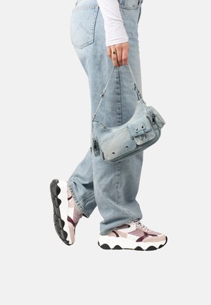 Light blue denim shoulder bag with zippered pockets, finished with soft texture and metal hardware. Worn with light blue jeans and chunky sneakers.
