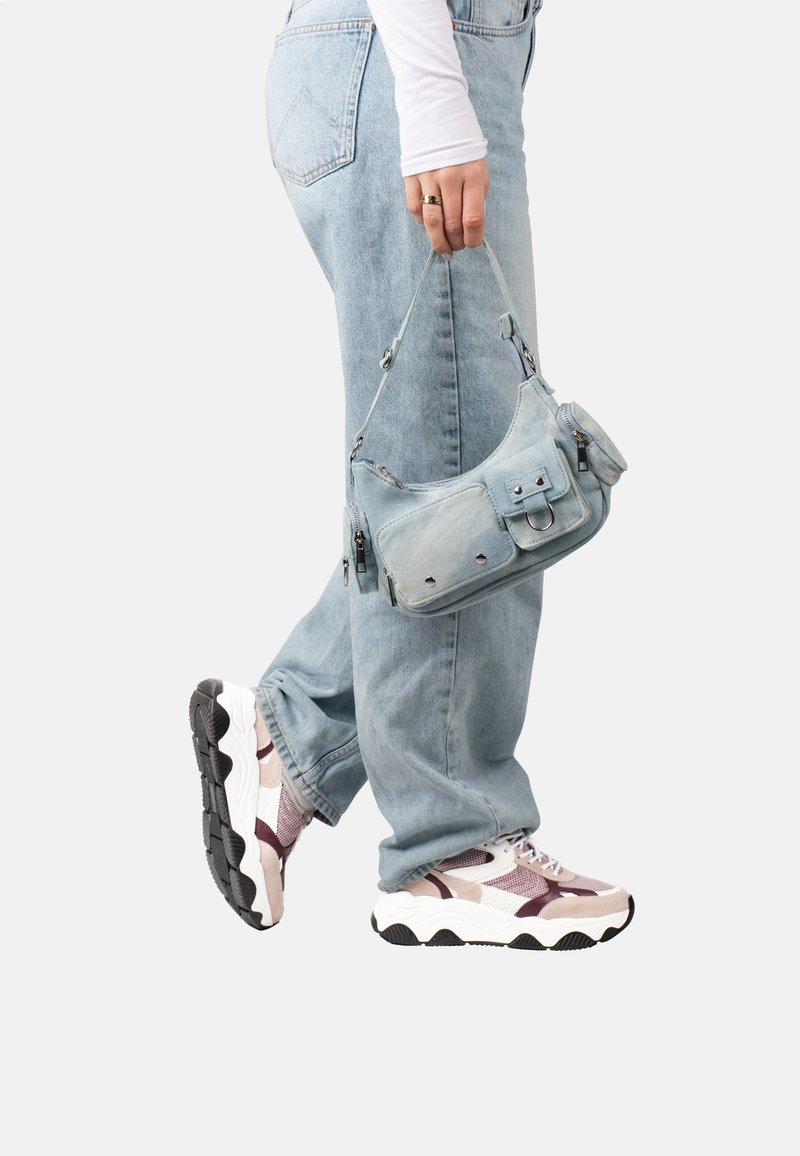 Sac à bandoulière en denim bleu clair avec poches zippées, fini avec une texture douce et des accessoires en métal. Porte avec un jean bleu clair et des baskets larges.