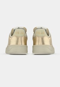 Χρυσά μεταλλικά αθλητικά παπούτσια με μπεζ λεπτομέρειες. Διαθέτουν υφή και άνετη σόλα. Το λογότυπο "VEJA" εμφανίζεται στην ταμπελίτσα της φτέρνας.