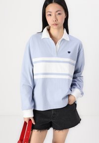 Svetlo modra polo majica z dolgimi rokavi z belimi črtami in majhno detajlom srca. Ima bel ovratnik in rebraste manšete. Črni denim kratki hlače.