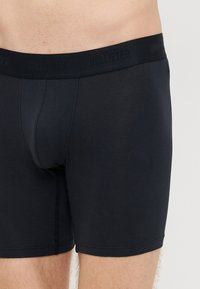 Fekete boxeralsó, puha, rugalmas anyagból, márkázott elasztikus derékrésszel és testhezálló szabással. Elülső nyílással rendelkezik.