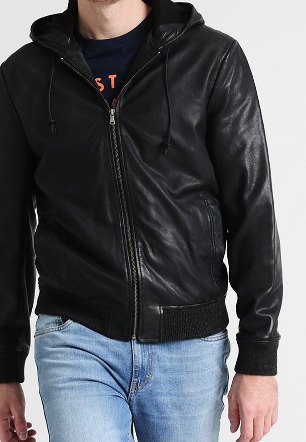 Giacca nera in pelle con cappuccio, con zip frontale, polsini e orlo a costine, e una texture liscia. Indossata sopra una t-shirt scura e jeans blu.